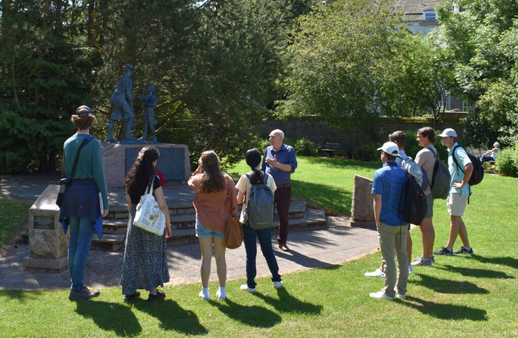 group of people gathering in front of a statue and listening to a tour guide.