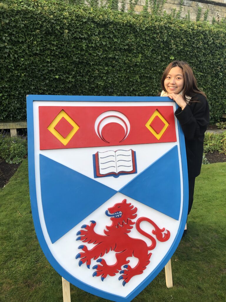 Person posing with a large university logo shield.