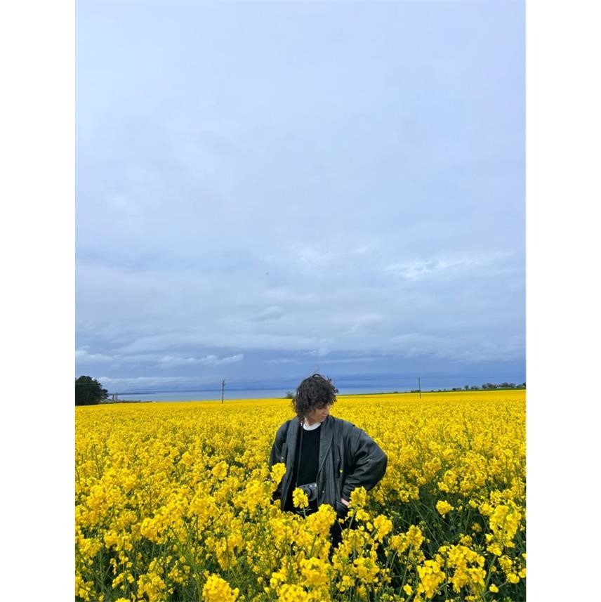 Agata stands in a large field of yellow blooming flowers with camera around the neck, ready to explore Scotland.