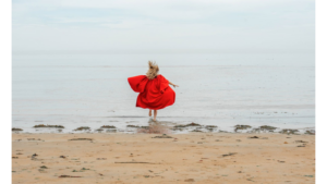 Student in red St Andrews gown running on the beach
