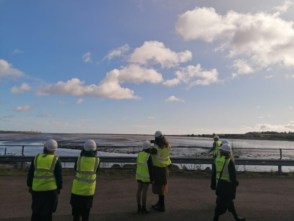 People in hard hats and high viisbility jackets look over an estuary view