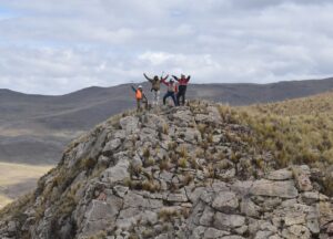 Four people standing on a mountain in Peru with arms raised.