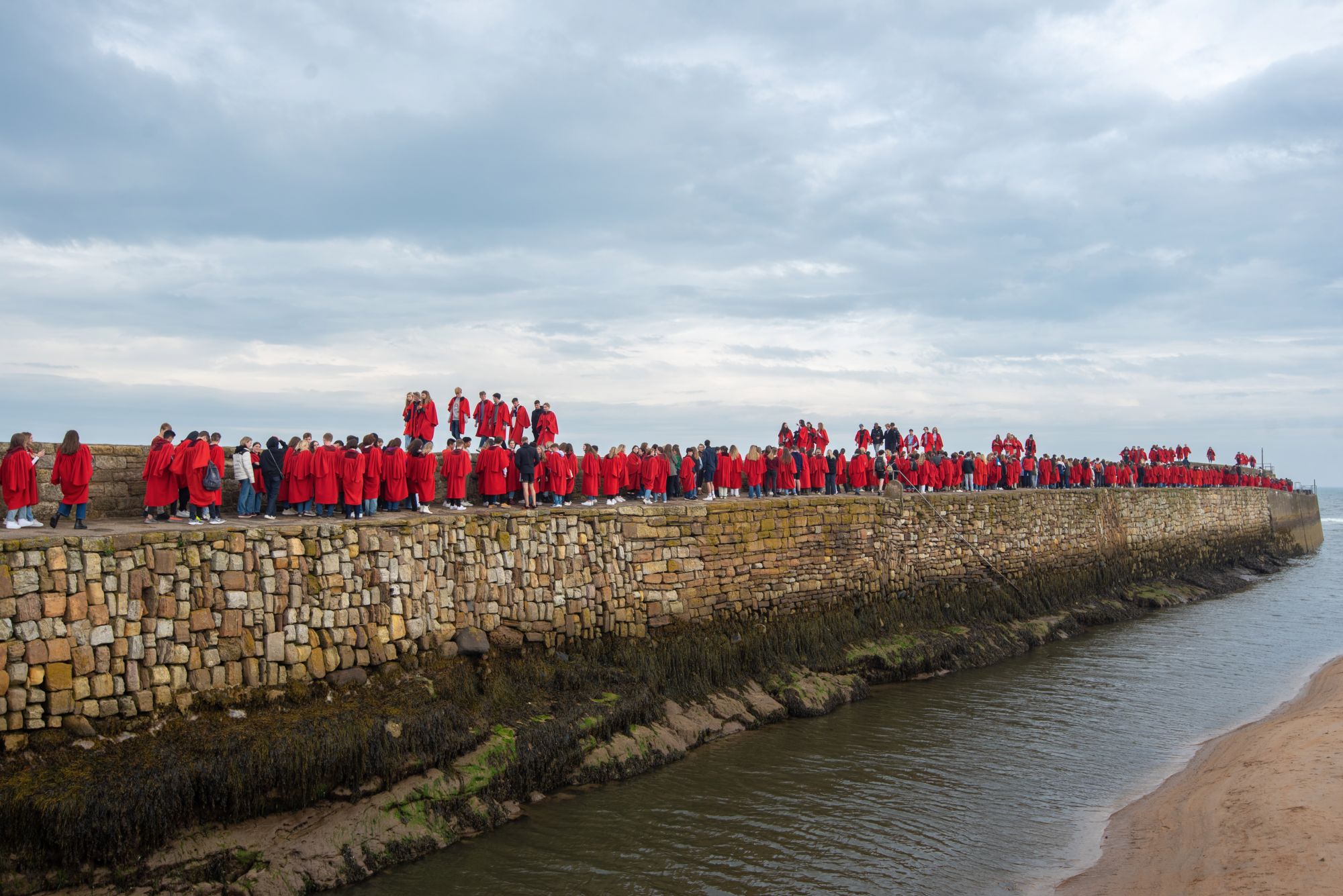 Students walking along the pier in their red gowns.