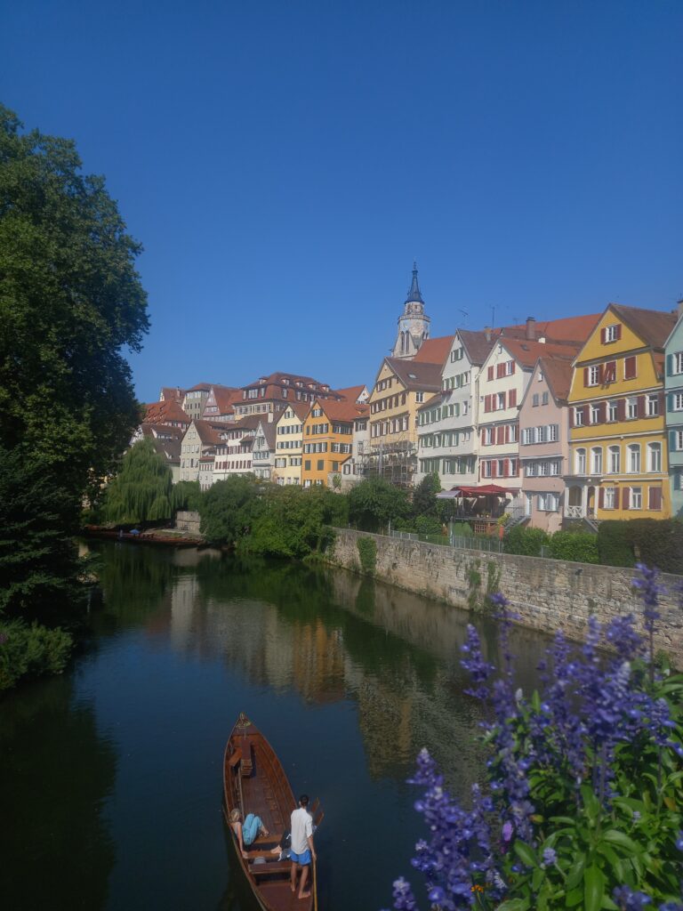 The colourfully painted riverside houses of Tubingen, with flowers and people in a rowing boat in the foreground.