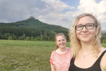 Image of two students on the right, and Hohenzollern castle perched on a wooded hill.