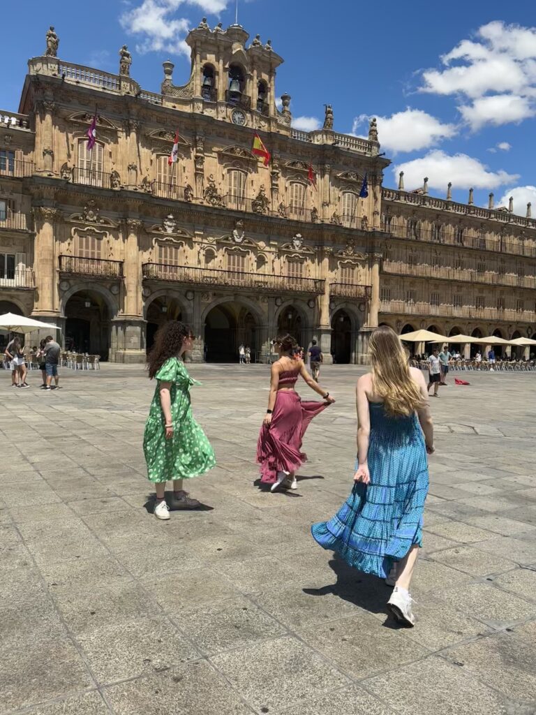 Students in colourful clothes stand in front of the baroque square in Salamanca.