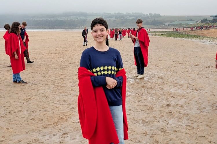 Student in a red robe standing on the beach