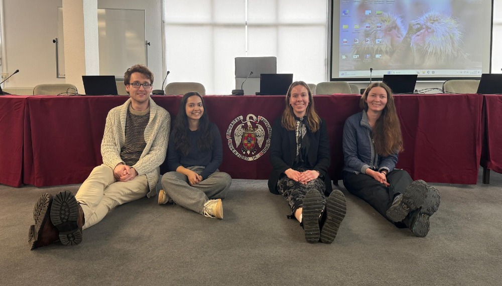Group of 4 students sitting in front of a presentation screen, with Complutense University of Madrid emblem.