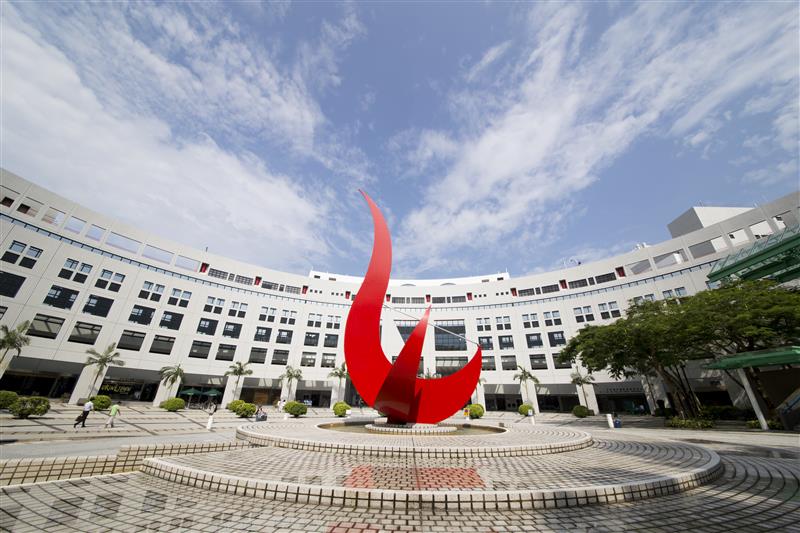 A large red scultpture, in an abstract bird form, in the centre of a plaza surrounded by modern buildings.
